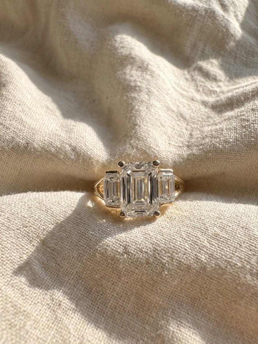 Gold ring with emerald-cut diamonds on a beige fabric background